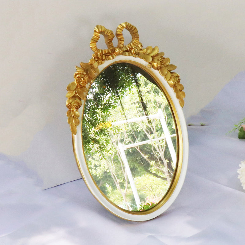 Oval gold decorative mirror with bow and floral accents. A vintage-inspired tabletop mirror perfect for elegant and romantic home decor.